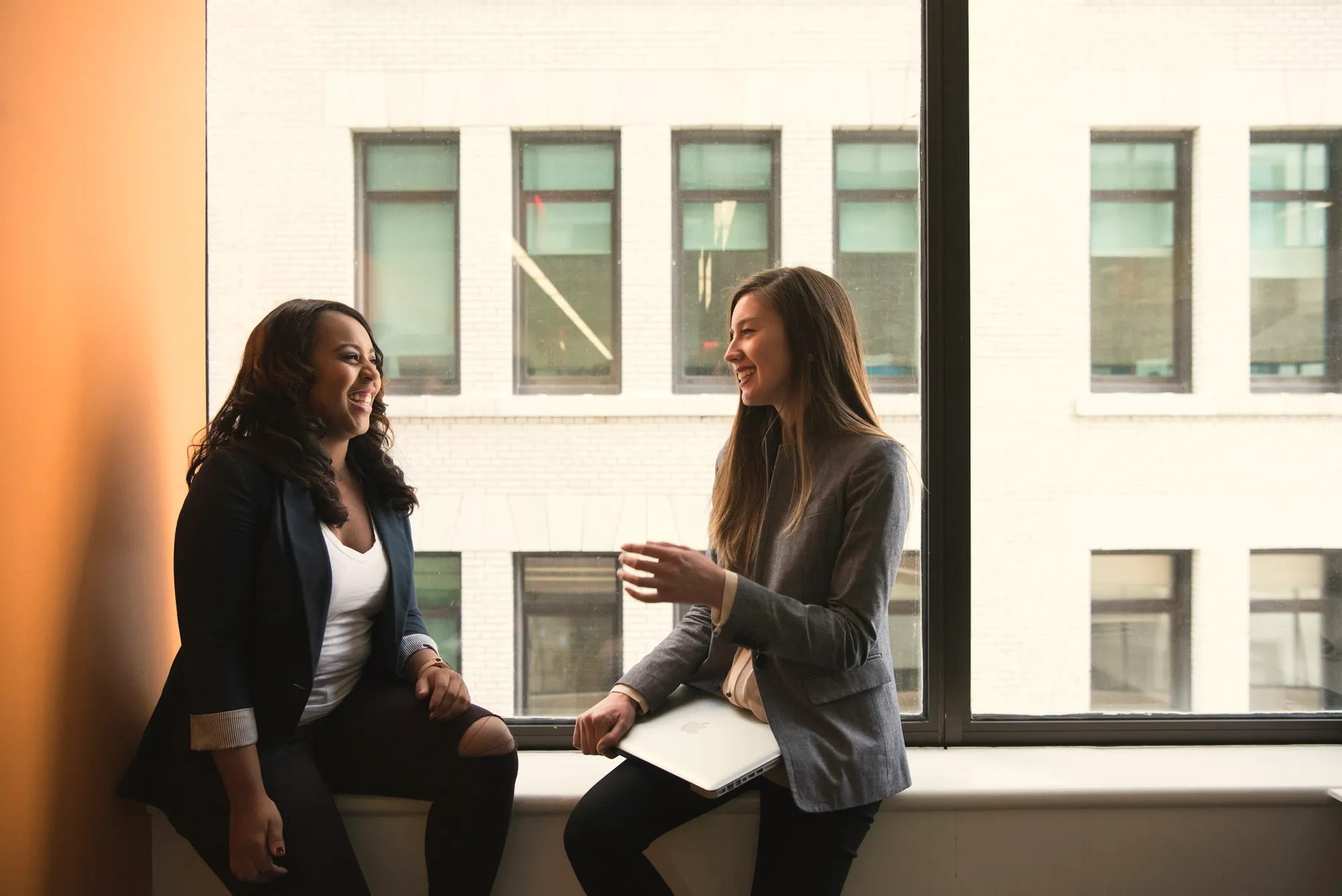Two colleagues laugh together by a window